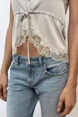 Top satinado color celeste con escote en pico y tirantes finos. Presenta detalles de encaje gris en el escote y el bajo, y una cintura ajustable con lazada.