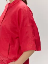 Chaqueta de lino y rayón color tostado, de corte holgado, mangas cortas amplias, cuello mao y cierre frontal oculto con cremallera. Presenta pespuntes a contratono en las costuras y cordón ajustable en el bajo.