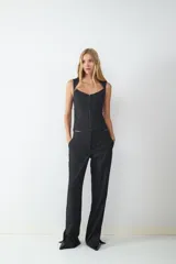 Pantalón de tiro medio color negro con raya diplomática, corte recto, bolsillos laterales con cierre y cierre frontal oculto. Presenta aberturas en los tobillos.