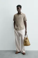 Camisa de lino color beige de corte relajado, con cuello solapa, manga corta y cierre frontal con botones.