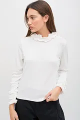 Polera de manga larga color azul jaspeado, con cuello alto y puños decorados con volados. Presenta un calce cómodo y relajado.