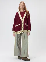 Cardigan de punto trenzado en color negro con detalles en color crema en los bolsillos, puños y ruedo. Presenta un diseño oversize, cierre frontal con botones y bordado decorativo en uno de los bolsillos delanteros.