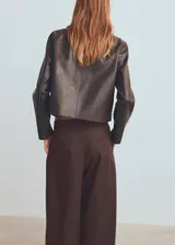 Chaqueta de piel sintética en color marrón, de diseño recto, manga larga y cuello con solapa. Cuenta con cierre frontal de botones, dos bolsillos laterales y forro interior.