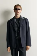 Blazer de corte relaxed fit con cuello de solapas de muesca y cierre frontal de un botón. Cuenta con bolsillos de plastrón en la cadera y mangas largas.