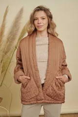 Campera tipo kimono acolchada en color marrón, con diseño de pespuntes verticales en el cuello y rombos en el cuerpo. Presenta mangas largas con puños vueltos y bolsillos frontales amplios.
