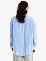 Camisa celeste y blanca a rayas verticales, de corte holgado, con cuello clásico, bolsillo en el pecho, mangas largas con puños blancos y cierre frontal con botones.