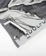 Chal jacquard de algodón orgánico con diseño estampado en tonos grises y blancos, logo de la marca y remates desflecados en los extremos.