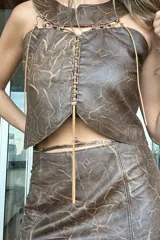Top corto de cuero ovino marrón con efecto veteado, diseño sin mangas con cuello redondo y detalles de pasamanería en la unión de las piezas.