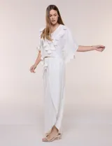 Blusa blanca de silueta holgada con sutil trama en hilo metalizado lurex, escote en V con pechera tejida en crochet y apliques de borlas en el contorno del cuello y las mangas.