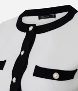 Cardigan de punto de manga corta con cuello redondo y cierre frontal de botones perolados. Presenta un diseño bicolor en blanco y negro con detalles de contraste en cuello, puños, tapetas de bolsillos frontales y vista central.