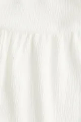 Pantalón blanco de corte globo con cintura ancha fruncida y bajos elásticos. El tejido presenta una textura arrugada.