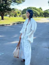 Camisa larga tipo sobrecamisa o abrigo ligero, color verde menta pálido con estampado floral en tono amarillo claro. Presenta escote en V con atado frontal mediante lazos, mangas largas con detalle fruncido y puños con flecos en tono turquesa.