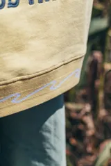 Hoodie amarillo con capucha, de corte holgado y diseño de espalda con bordado gráfico de olas, sol y la inscripción 'Glassy Waves'. Presenta detalles de ondas bordadas en el ruedo inferior.