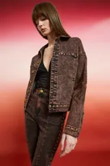 Campera de jean con lavado oscuro rojizo/marrón, estilo trucker. Presenta tachas doradas a lo largo de los bordes de los bolsillos, el canesú y los puños. Posee un bordado en relieve de diseño floral en la manga.