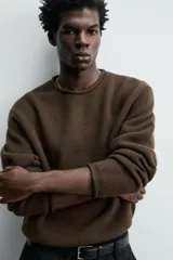 Jersey de punto de lana color marrón oscuro, de calce regular y manga larga, con cuello redondo y acabados enrollados en puños y ruedo.