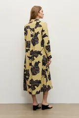Vestido camisero midi de color amarillo maíz con estampado floral en tonos oscuros, de manga larga, cuello camisero, cierre frontal de botones y cinturón negro delgado con hebilla metálica.