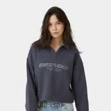 Polo crewneck de EmeStudios en color azul marino, con cuello tipo polo sin botones y mangas largas de caída amplia. Presenta el logo de la marca y un mensaje bordado en el frente en tono sobre tono.