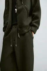 Pantalón de corte wide fit confeccionado en tejido técnico con efecto neopreno. Presenta cintura elástica ajustable con cordón, perneras anchas con costura frontal, bolsillos laterales y bolsillos traseros de plastrón.