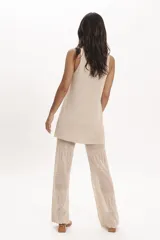 Pantalón de tejido de punto negro, corte ancho y tiro alto, con detalle de encaje calado en la parte inferior. Se lleva debajo de un vestido largo de encaje negro con tirantes finos y botones frontales.