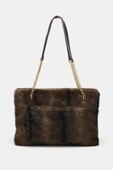 Bolso de hombro con cuerpo de textura efecto pelo en color marrón oscuro. Cuenta con un asa de hombro combinada con cadena metálica dorada, bolsillo exterior frontal y cierre principal mediante cremallera.