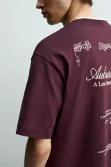 Camiseta de corte relajado color bordó, con cuello redondo y manga corta. Presenta un pequeño texto bordado en contraste en el pecho.