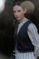 Chaleco de algodón color gris oscuro con bordados coloridos en contraste y ribetes en azul y amarillo. Presenta cierre frontal con tiras para atar.