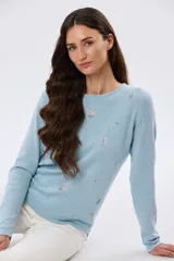 Buzo tejido de algodón color celeste, de manga larga y cuello redondo, con delicados bordados florales distribuidos en el frente y las mangas.