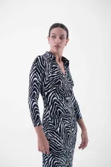 Vestido midi de corte ajustado, con estampado animal print tipo cebra en blanco y negro, cuello camisero, escote en V y cierre frontal con botones dorados.