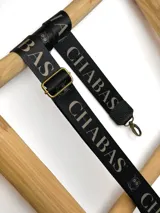 Correa ajustable para cartera confeccionada en cinta tejida con diseño de rayas en negro, blanco y beige, con punteras de cuero sintético negro y herrajes metálicos.