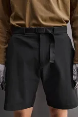 Bermuda de ajuste regular color marrón oscuro, confeccionada en tejido técnico compacto con elasticidad. Presenta cintura ajustable con cinturón negro a contraste, bolsillos frontales y un bolsillo cargo con cierre de cremallera oculta en la pernera.