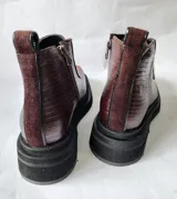 Botas cortas marca Lanka, confeccionadas en cuero vacuno color chocolate. Presentan una combinación de texturas, con paneles laterales de cuero grabado tipo reptil y frente liso. Cuentan con cierre frontal, puntera cuadrada y suela de plataforma dentada en color negro.