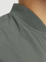 Campera bomber verde militar, liviana, de manga larga con cuello baseball y corte cómodo. Tiene cierre frontal de cremallera, bolsillos delanteros y puños de canalé.