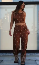 Conjunto de dos piezas compuesto por un top corto tipo strapless y un pantalón de corte holgado, ambos en color marrón con estampado geométrico étnico. El pantalón presenta un diseño de pierna ancha con detalle de guarda decorativa en el ruedo.