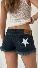 Short de jean tiro bajo color azul oscuro, con diseño de estrella blanca estampada en el bolsillo trasero y terminaciones desflecadas en las piernas.