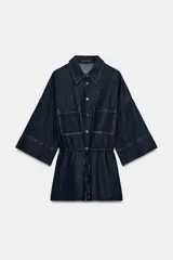 Camisa de denim azul oscuro con cuello solapa, mangas amplias por debajo del codo y bolsillos de parche en el frente. Cuenta con cintura ajustable mediante cordón y cierre frontal con botones metálicos.
