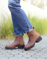 Botinetas de cuero color marrón con diseño combinado en cuero liso y gamuza. Presentan suela track de goma negra con taco cuadrado y tirador en la parte trasera.