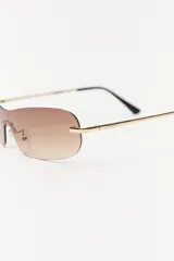 Lentes de sol con lentes marrones degradé sin marco y patillas doradas.