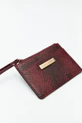 Billetera rectangular color bordó con estampado de piel de serpiente, cierre superior con cremallera, bolsillo frontal y correa de muñeca.
