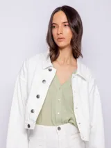 Campera corta de jean color blanco, con cuello camisero, botones metálicos plateados en el frente y puños, y bolsillos delanteros con solapa.