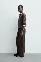 Pantalón chino de corte wide fit confeccionado en tejido de algodón. Presenta pliegues frontales, bolsillos laterales y bolsillos traseros de vivo, con cierre frontal de cremallera y botón.