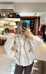 Camisa de manga larga color marrón oscuro, con cuello camisero y botones frontales claros. Presenta un calce holgado y mangas abullonadas con puños ajustados.