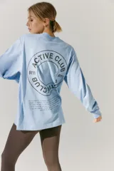 Remerón de manga larga color celeste, con cuello redondo y puños acanalados. Presenta una estampa circular en la espalda con el texto 'ACTIVE CLUB' y detalles de texto adicional en la parte inferior.