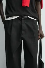 Pantalón de corte balloon fit y estilo relajado, confeccionado en tejido de algodón. Presenta pliegues frontales, cintura con trabillas, cierre frontal con cremallera y botón, bolsillos delanteros y bolsillos traseros de vivo.