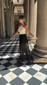 Falda larga de encaje negro con diseño de capas, presentando una sección superior opaca y una sección inferior transparente con terminación de volado en el ruedo.