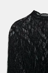 Top negro de encaje con cuello redondo, manga larga acampanada y bajo recto.