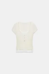 Camiseta efecto doble en color crudo y blanco, de manga corta y corte slim fit. Cuenta con escote redondo, cierre frontal parcial con botones a presión y diseño de capas superpuestas.