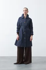 Trench de diseño clásico en color beige, con cierre frontal de botones, cinturón ajustable con hebilla a tono y mangas con trabillas en los puños.