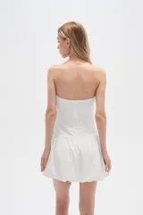 Vestido corto strapless de color blanco, con diseño drapeado en el torso y falda estilo globo con ruedo voluminoso.