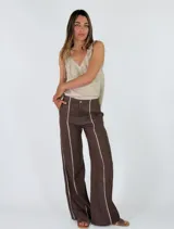 Pantalón marrón de lino de corte recto y holgado, con costuras decorativas claras a lo largo de las piernas.
