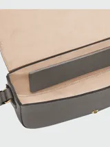 Cartera tipo bandolera de cuero granulado en color gris, con diseño de solapa redondeada y cierre de broche metálico dorado. Incluye correa larga ajustable para llevar al hombro o cruzada.